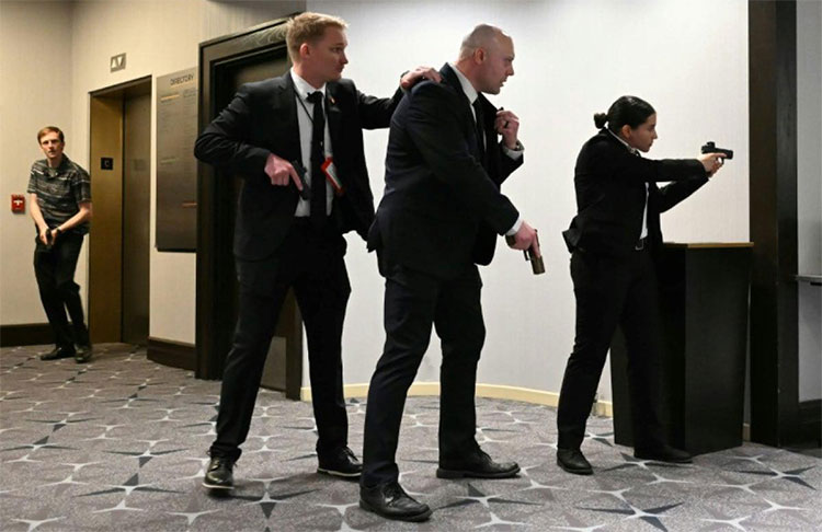 အမေရိကန် သမ္မတ ဒေါ်နယ်ထရန့် တက်ရောက်တဲ့ ညစာစားပွဲမှာ ပစ်ခတ်မှု ဖြစ်ပွား   သတင်းနဲ့ မီဒီယာ ကွန်ရက်။  ၂၀၂၆ ခုနှစ်၊ ဧပြီလ ၂၆ ရက်။   ဝါရှင်တန်ဒီစီရဲ့ ခမ်းနားထည်ဝါလှတဲ့ စနေနေ့ညချမ်းဟာ ရုတ်တရက်ဆိုသလို ထိတ်လန့်တုန်လှုပ်ဖွယ်ရာ အခိုက်အတန့်တွေနဲ့ ပြည့်နှက်သွားခဲ့ပါတယ်။   ဝါရှင်တန်ဟီလ်တန်ဟိုတယ်မှာ ကျင်းပနေတဲ့ အိမ်ဖြူတော်သတင်းထောက်များအသင်း (WHCA) ရဲ့ နှစ်ပတ်လည်ညစာစားပွဲမှာ သေနတ်သံလိုမျိုး ကျယ်လောင်တဲ့ အသံတွေထွက်ပေါ်လာပြီးနောက် သမ္မတ ဒေါ်နယ်ထရန့်ကို လုံခြုံရေးအဖွဲ့ဝင်တွေက အရေးပေါ် ဘေးကင်းရာကို ခေါ်ဆောင်သွားခဲ့ရပါတယ်။   ဖြစ်စဉ်ဖြစ်ပွားခဲ့ပုံ   ဝါရှင်တန်ဟီလ်တန်ဟိုတယ်ရဲ့ ခမ်းမကြီးအတွင်းမှာတော့ တီးဝိုင်းရဲ့ သံစဉ်တွေ၊ ဝတ်စုံပြည့်ဝတ်ဆင်ထားတဲ့ အစိုးရအဖွဲ့ဝင်တွေနဲ့ သတင်းထောက်တွေရဲ့ ရယ်မောသံတွေကြောင့် စည်ကားလို့နေတယ်လို့ အဲဒီပွဲမှာ တက်ရောက်နေတဲ့ သတင်းထောက်တွေက ပြန်ရေးကြပါတယ်။     သမ္မတ ဒေါ်နယ်ထရန့်ဟာ သမ္မတသက်တမ်းအတွင်း ပထမဆုံးအကြိမ်အဖြစ် ဒီညစာစားပွဲကို တက်ရောက်လာတာဖြစ်ပြီး စင်မြင့်ထက်မှာ ဂုဏ်သရေရှိလူကြီးမင်းတွေနဲ့အတူ နေရာယူထားခဲ့ပါတယ်။   ဒါပေမယ့်လည်း ပျော်ရွှင်စရာကောင်းနေတဲ့ အခိုက်အတန့်ဟာ ကျယ်လောင်လှတဲ့ အသံဗလံတွေကြောင့် ရုတ်ချည်းပျက်ပြယ်သွားခဲ့ပါတယ်။   ခန်းမထဲက ဧည့်သည်တွေဟာ "ဝပ်နေကြ! အောက်ဆင်းနေကြ!" ဆိုတဲ့ အော်ဟစ်သံတွေနဲ့အတူ ကြမ်းပြင်ပေါ်ကို မှောက်ချလိုက်ကြရပါတယ်။   "ကျွန်မ စားပွဲအောက်ကိုပဲ ငုပ်လျှိုးနေလိုက်တော့တယ်။ ဘာဖြစ်နေလဲဆိုတာ မသိရတဲ့အတွက် အန္တရာယ်ကို မစွန့်စားနိုင်ဘူးလေ" လို့ One America News သတင်းထောက် Alexandra Ingersoll က အခြေအနေကို ပြန်ပြောင်းပြောပြပါတယ်။   အသံတွေထွက်ပေါ်လာပြီး စက္ကန့်ပိုင်းအတွင်းမှာပဲ လျို့ဝှက် လုံခြုံရေး Secret Service တပ်ဖွဲ့ဝင်တွေဟာ လက်နက်တွေကိုယ်စီနဲ့ သမ္မတကို ဝိုင်းရံလိုက်ကြပြီး စင်နောက်ဘက်ကတစ်ဆင့် ဘေးကင်းရာကို အမြန်ဆုံး ခေါ်ဆောင်သွားခဲ့ပါတယ်။   အဲဒီ အချိန်မှာတော့ ခန်းမထဲက ဂီတသံတွေ ရပ်တန့်သွားပြီး ကြောက်လန့်တုန်လှုပ်နေတဲ့ ဧည့်သည်တွေကြားထဲမှာ လုံခြုံရေးအေးဂျင့်တွေဟာ သေနတ်တွေကိုင်ဆောင်ပြီး နေရာအနှံ့ ဖြန့်ကြက်စစ်ဆေးခဲ့ကြပါတယ်။     ထူးခြားတဲ့ တိုက်ဆိုင်မှုတစ်ခုကတော့ ဒီဟိုတယ်ဟာ လွန်ခဲ့တဲ့ ၄၅ နှစ်က အမေရိကန် သမ္မတ ရော်နယ်ရေဂင် လုပ်ကြံသတ်ဖြတ်ခံရမှုကနေ ကံကောင်းထောက်မစွာ လွတ်မြောက်ခဲ့တဲ့ ဟော်တယ်ပဲ ဖြစ်နေပါတယ်။   ညစာစားပွဲကနေ ဘေးကင်းရာကို အရေးပေါ်ရွှေ့ပြောင်းပေးခဲ့ရသူတွေထဲမှာ ကျန်းမာရေးဝန်ကြီး Robert F. Kennedy Jr လည်း ပါဝင်ခဲ့ပါတယ်။ သူဟာ ၁၉၆၃ ခုနှစ်က လုပ်ကြံခံခဲ့ရတဲ့ သမ္မတ ဂျွန်အက်ဖ်ကနေဒီရဲ့ တူတော်စပ်သူဖြစ်ပါတယ်။   အဲဒီလိုပဲ သမ္မတရဲ့ အုပ်ချုပ်ရေးအဖွဲ့ဝင် တစ်ဦးဖြစ်တဲ့ Mehmet Oz ကလည်း အရေးပေါ်ထွက်ခွာသွားခဲ့ပါတယ်။   ဒီပစ်ခတ်မှု အတွင်းမှာ သမ္မတနှင့် သမ္မတကတော် လုံခြုံဘေးကင်းစွာ လွတ်မြောက်ခဲ့ပြိး အိမ်ဖြူတော်ကို ပြန်လှည့် သွားခဲ့ပါတယ်။   လုပ်ကြံ သတ်ဖြတ်ဖို့ ကြိုးစားခဲ့တယ်လို့ သံသယ ရှိသူ တစ်ဦးကို ဖမ်းဆီးထိန်းသိမ်းထားပါတယ်။   ဝါရှင်တန်ဟီလ်တန်ဟိုတယ် ပတ်ဝန်းကျင်မှာတော့ ရဲတပ်ဖွဲ့ဝင်တွေက လမ်းတွေကို ပိတ်ဆို့ပြီး လုံခြုံရေးအဆင့်မြှင့်တင်ထားသလို၊ ကောင်းကင်ယံမှာလည်း ရဟတ်ယာဉ်တွေနဲ့ ကင်းလှည့်နေပါတယ်။   #အမေရိကန်သမ္မတဒေါ်နယ်ထရမ့် #ပစ်ခတ်မှု #လုပ်ကြံမှု #ဝါရှင်တန်ဟီလ်တန်ဟိုတယ်